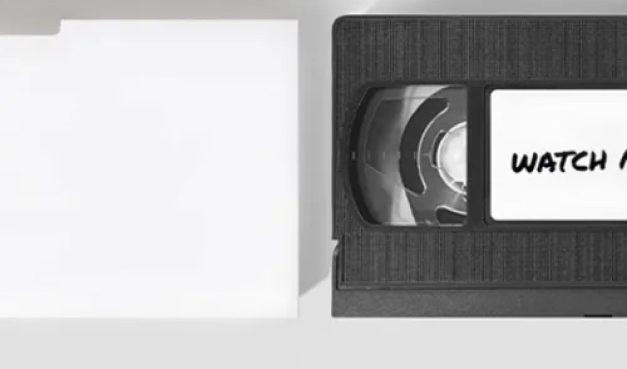 A top-down view of a video tape outside a case with the word "watch" written on it.