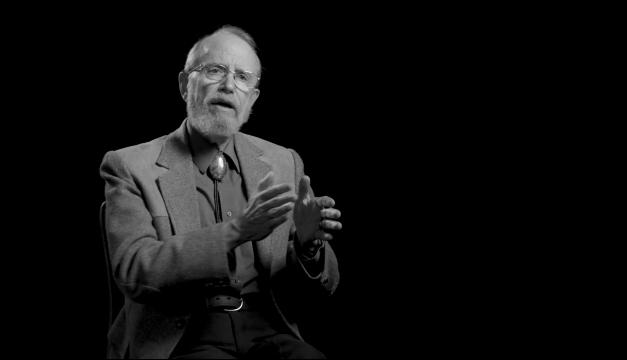 A black and white photo of Bill Miller with his hands raised mid-explanation.