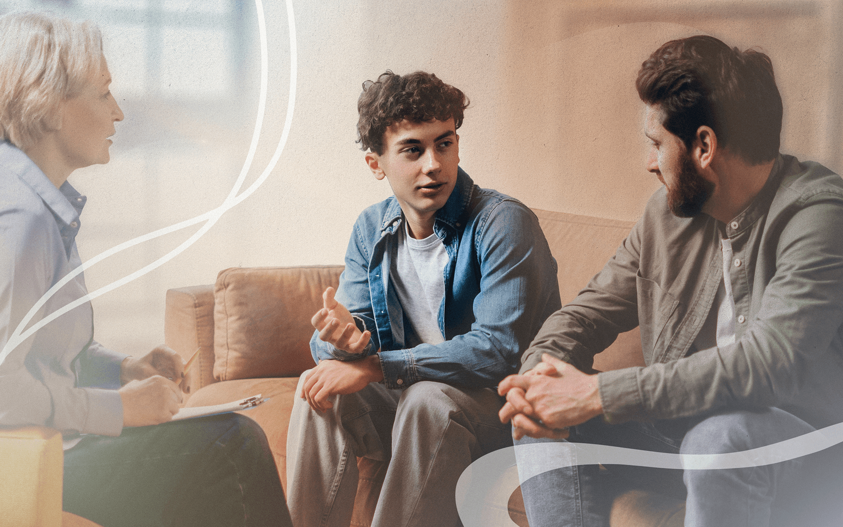 Three people are seated on a couch in a well-lit room. One person, a male with curly hair, is speaking and gesturing with his hands. The other two individuals, one male and one female, are listening attentively. The female is holding a notebook and pencil